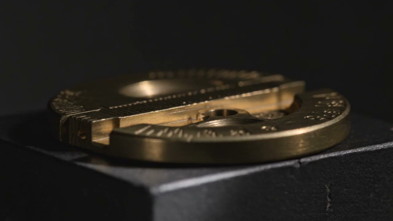 A single precision-machined brass component on a graphite surface.